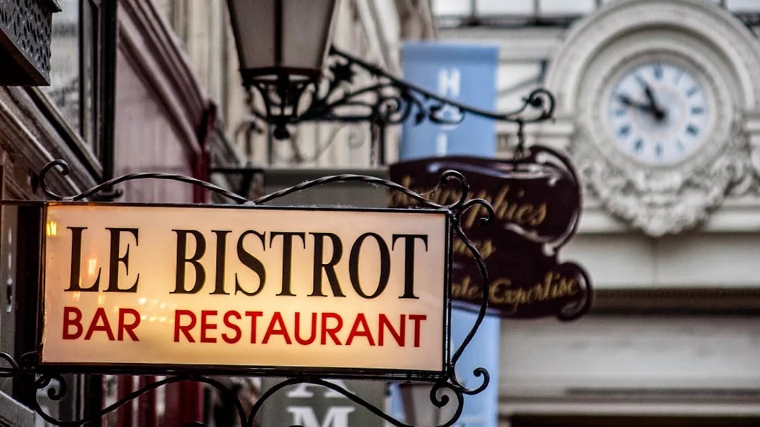 Le Bistrot sign in Paris covered passage with ornate clock in background.