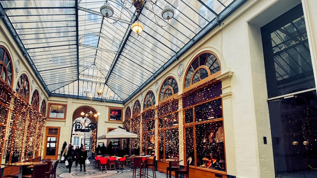 Covered passage in Paris with glass roof, arched windows, and people walking.
