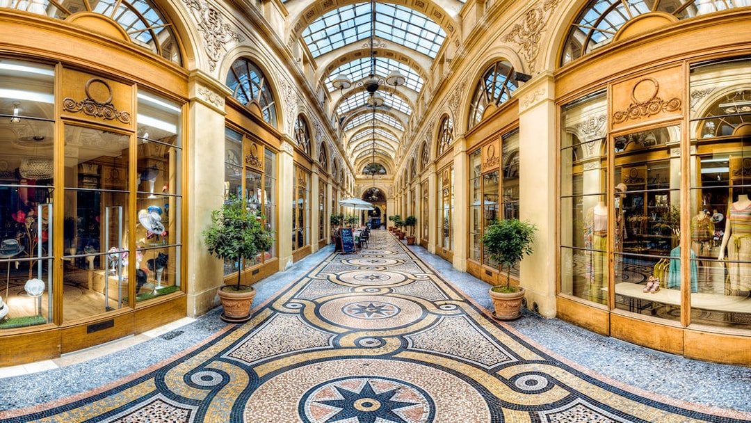 Covered passage in Paris with ornate glass ceiling and boutique shops.