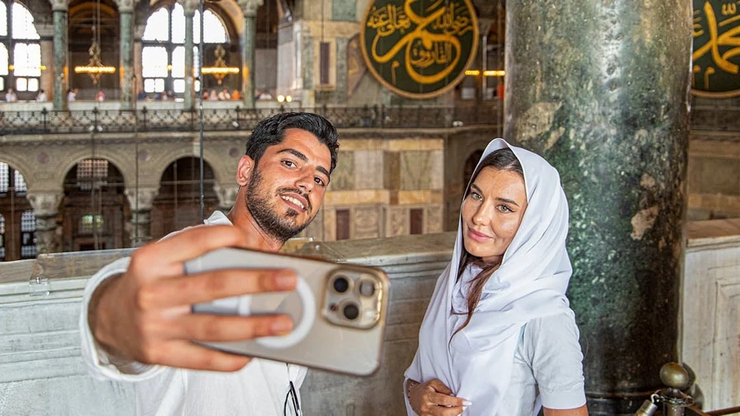 Visitors taking a selfie inside Hagia Sophia, Istanbul, with ornate interior details.