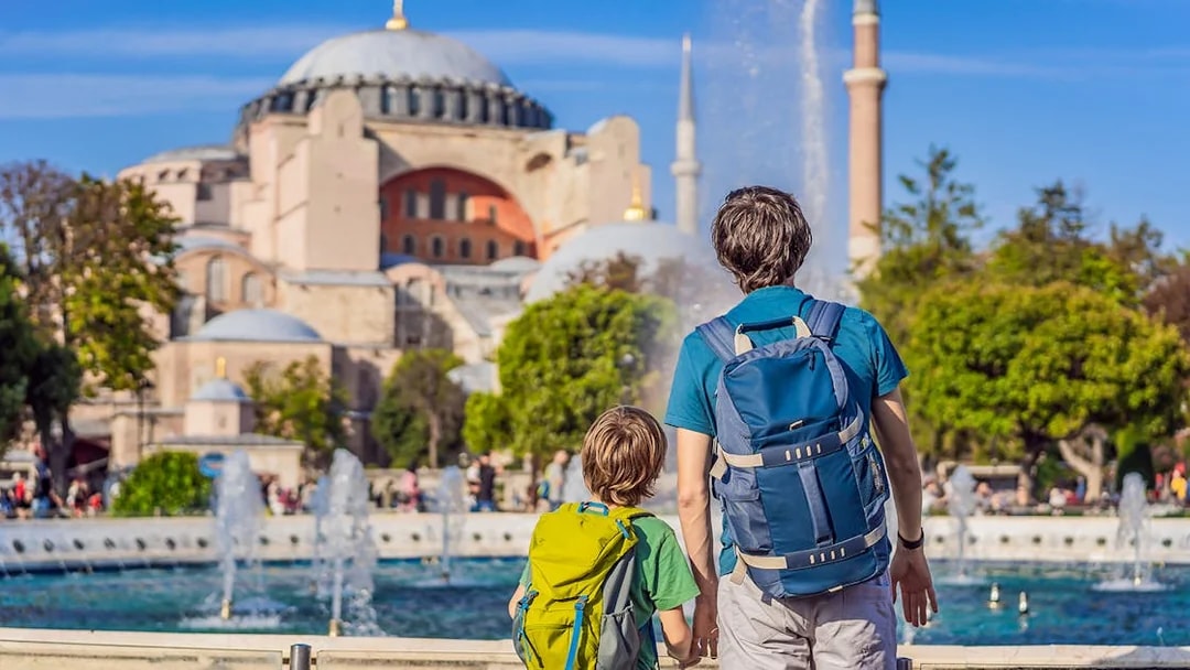 Tourists with backpacks viewing Hagia Sophia, Istanbul, near a fountain.