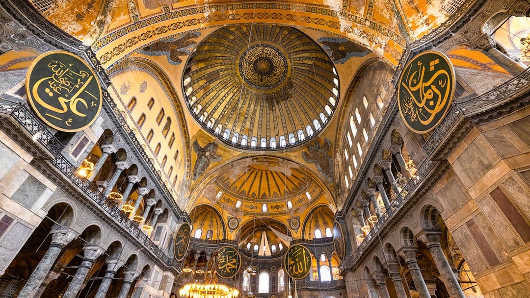 Interior view of Hagia Sophia's dome and arches in Istanbul, showcasing intricate mosaics and calligraphy.