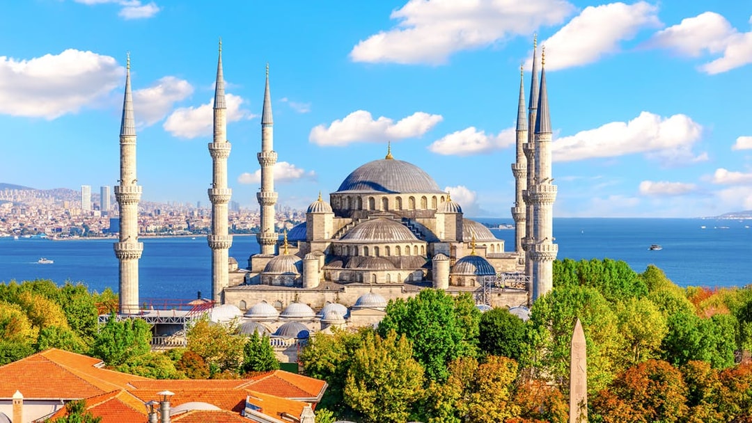 Blue Mosque exterior with minarets and domes, Istanbul skyline and Bosphorus in background.