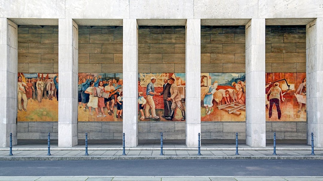 Berlin mural depicting historical scenes and workers at a memorial site.