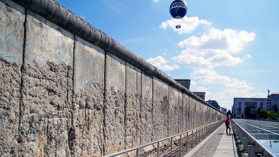 Berlin Wall with a hot air balloon in the sky and a person walking along the path.