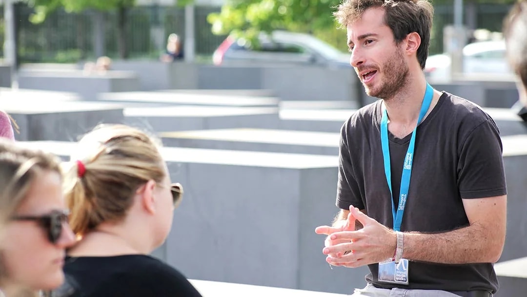 Tour guide explaining to tourists at an outdoor memorial site.