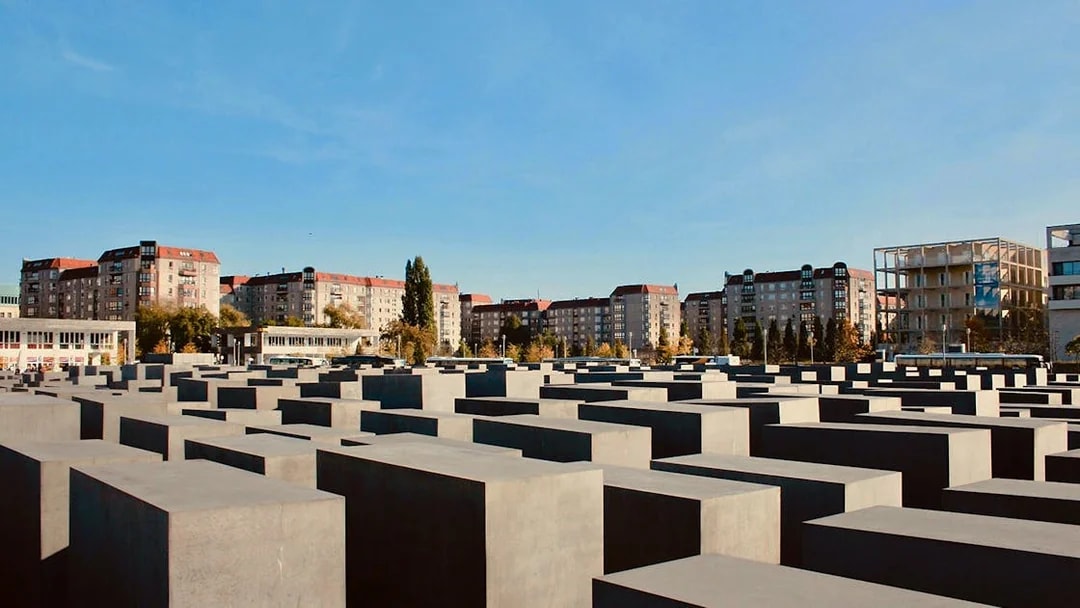 Holocaust Memorial in Berlin with concrete slabs and city buildings in the background.