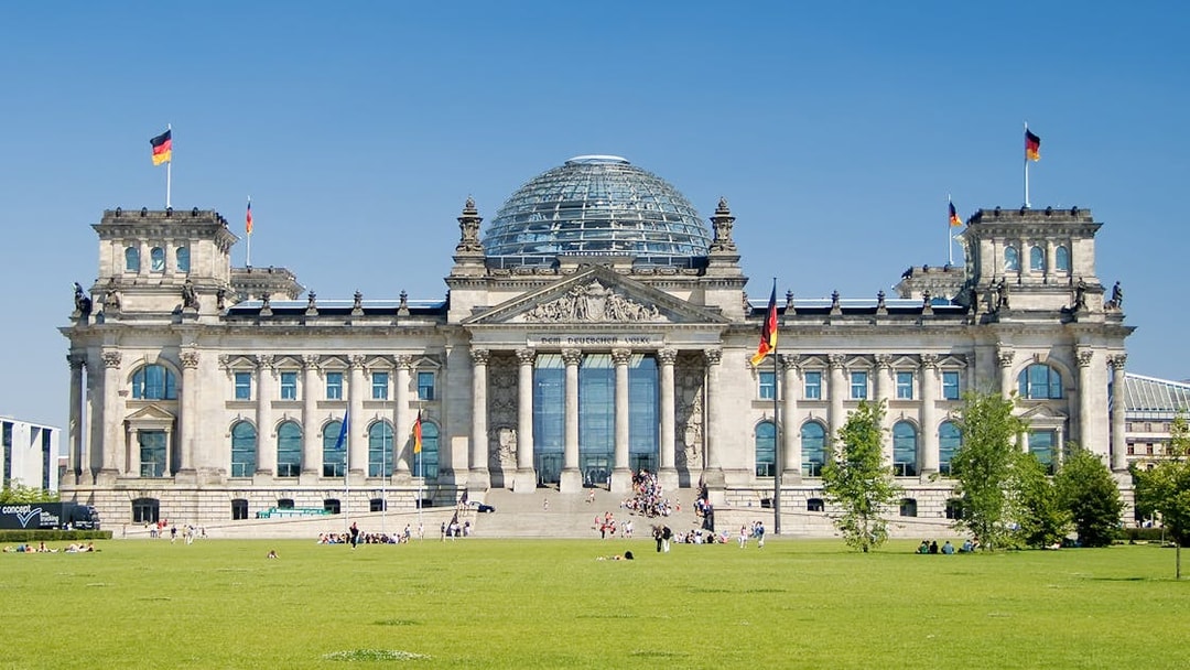Reichstag building in Berlin with glass dome and German flags.