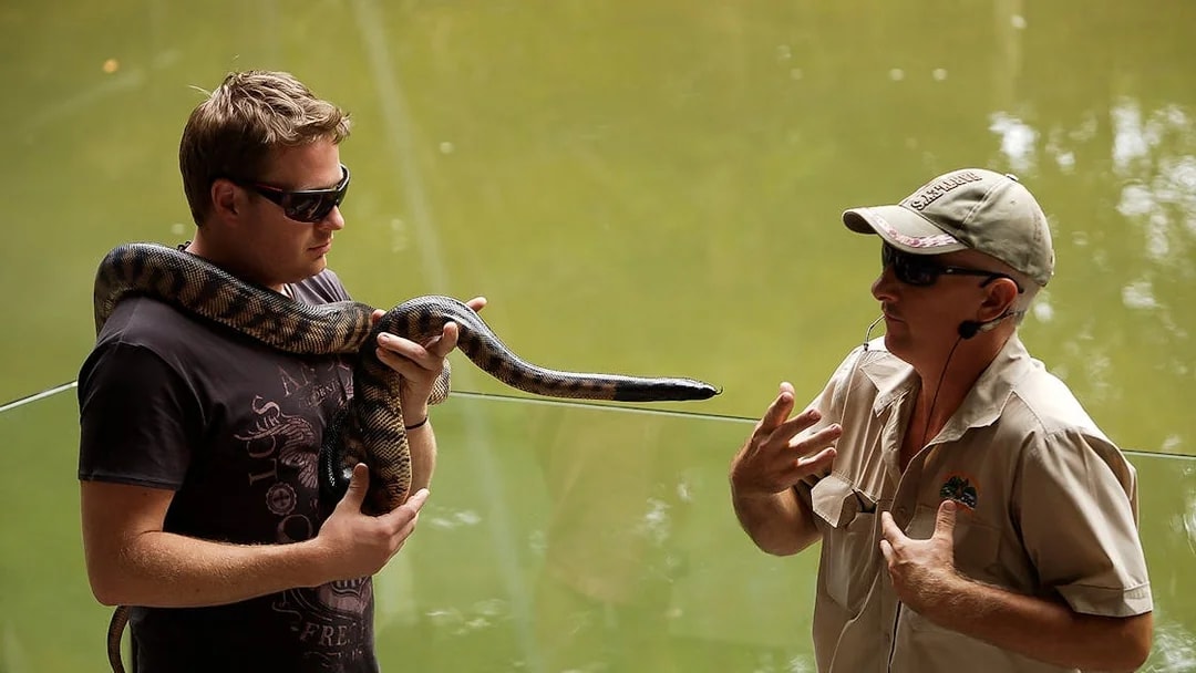 Man holding a snake with a guide at Hartley’s Crocodile Adventures.