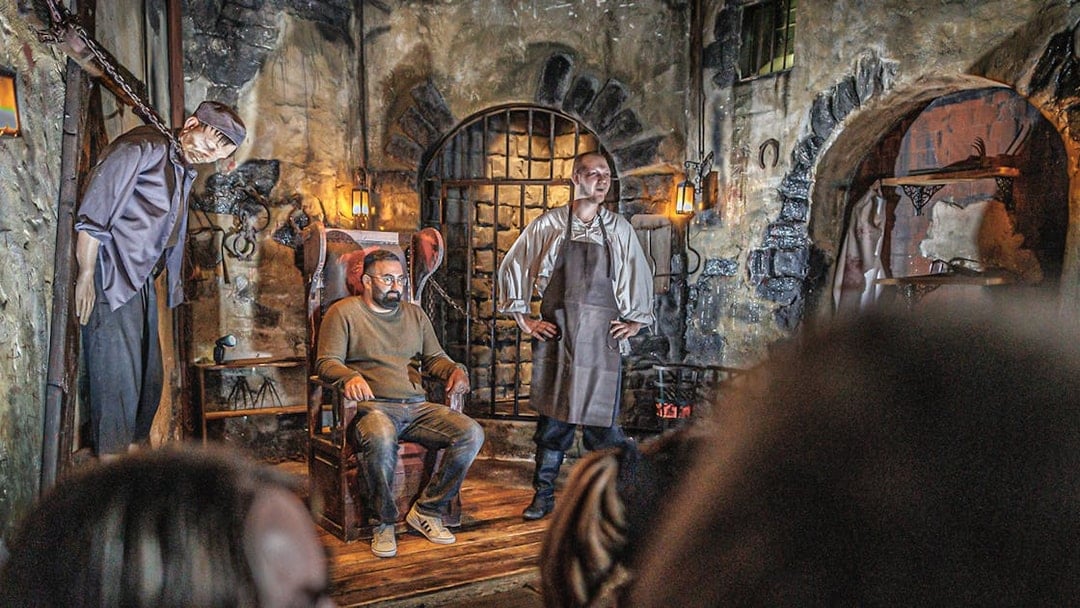 Torturer performing in Hamburg Dungeon with a visitor seated in a medieval setting.