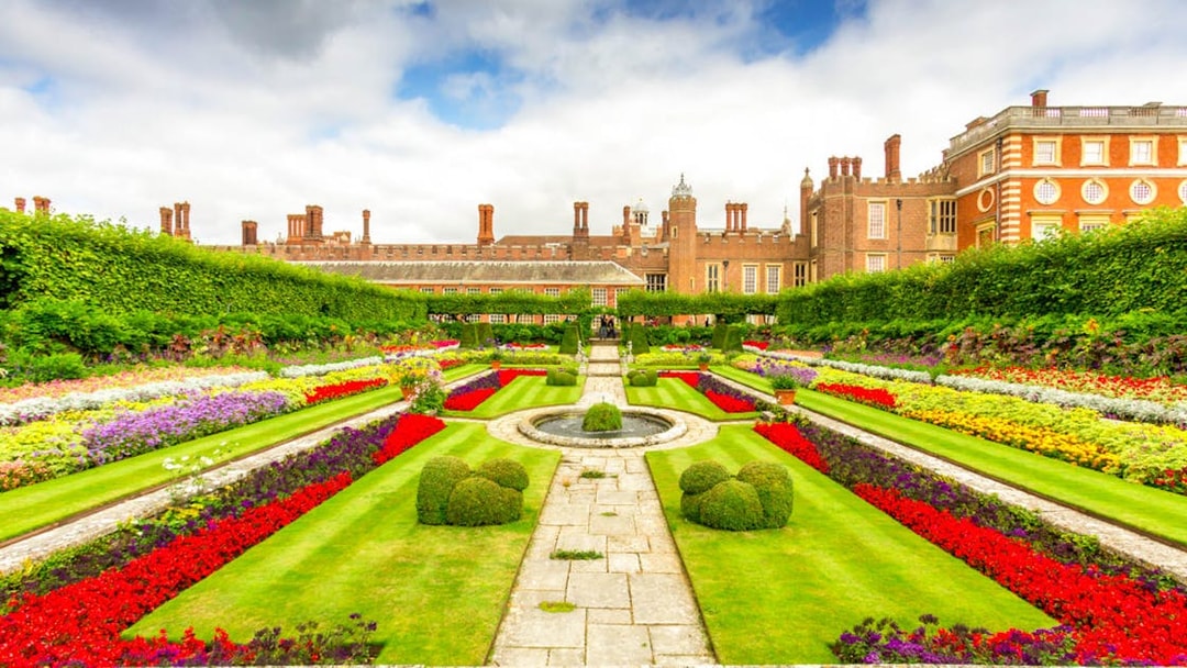 Hampton Court Palace gardens with colorful flower beds and historic architecture in the background.