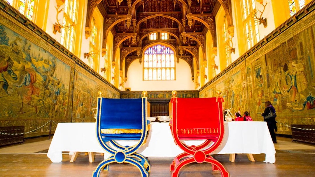 Visitors inside the Great Hall of Hampton Court Palace, London, viewing historic tapestries.