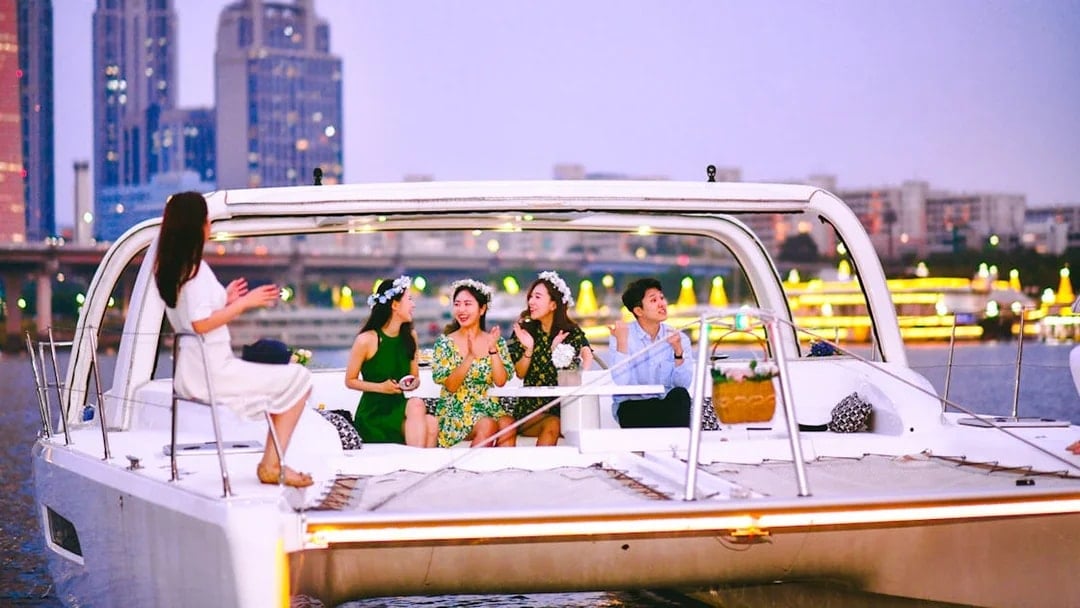 People enjoying a yacht cruise on the Han River in Seoul with city skyline in the background.