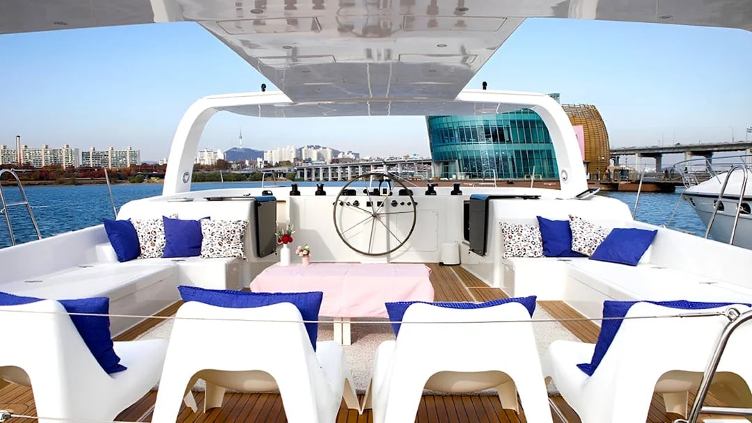 Yacht deck with seating area, blue cushions, and cityscape view in the background.