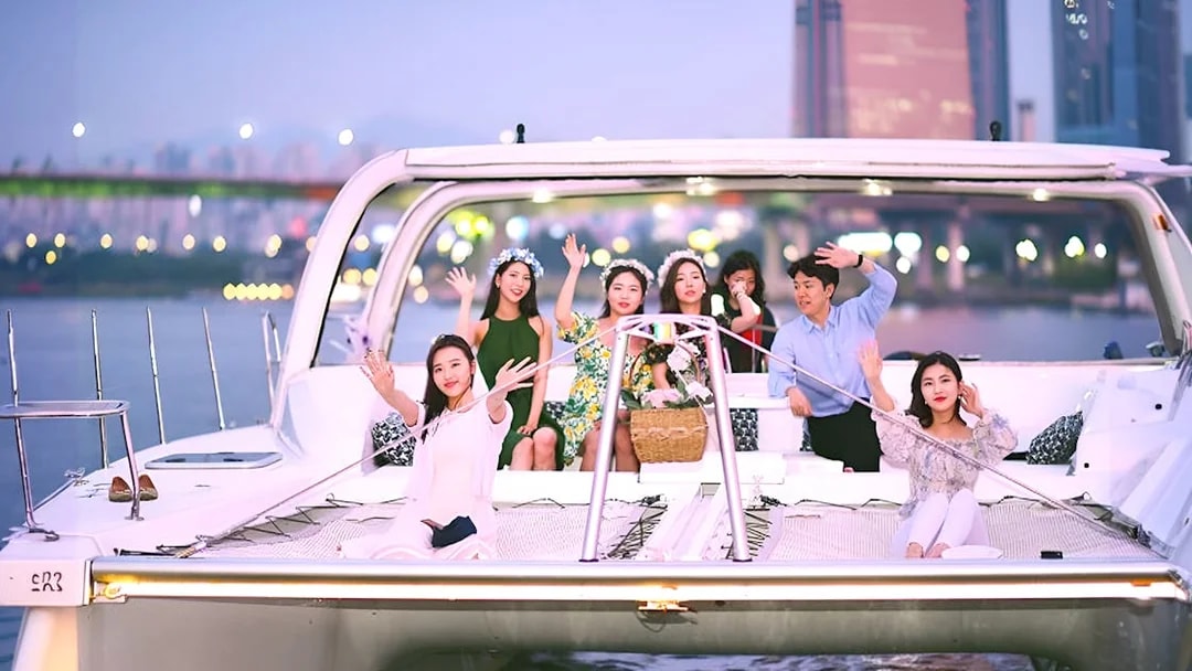 Group enjoying a yacht ride on the Han River, Seoul, with city lights in the background.