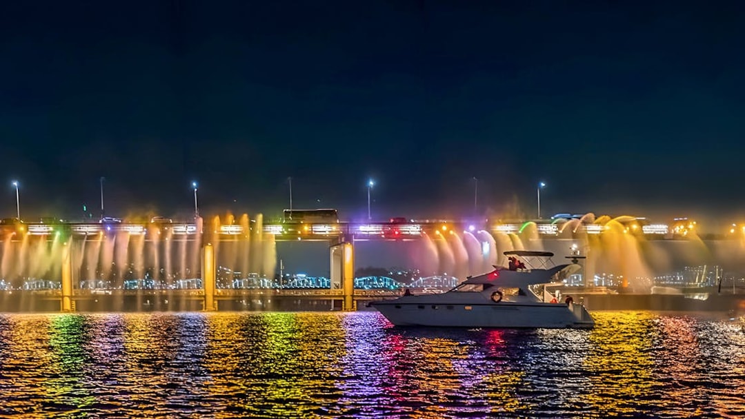 Yacht on Han River at night with colorful bridge lights in Seoul.