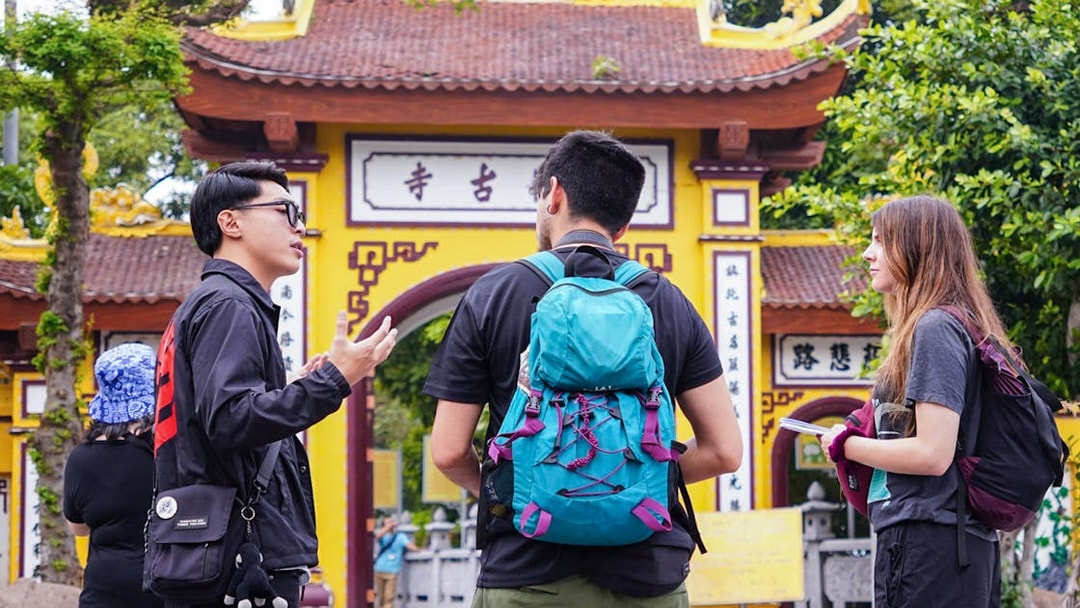 Tour guide with tourists at a historic temple entrance in Hanoi.