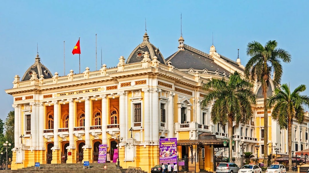 Hanoi Opera House with palm trees and cars in front, part of the Hanoi city highlights tour.
