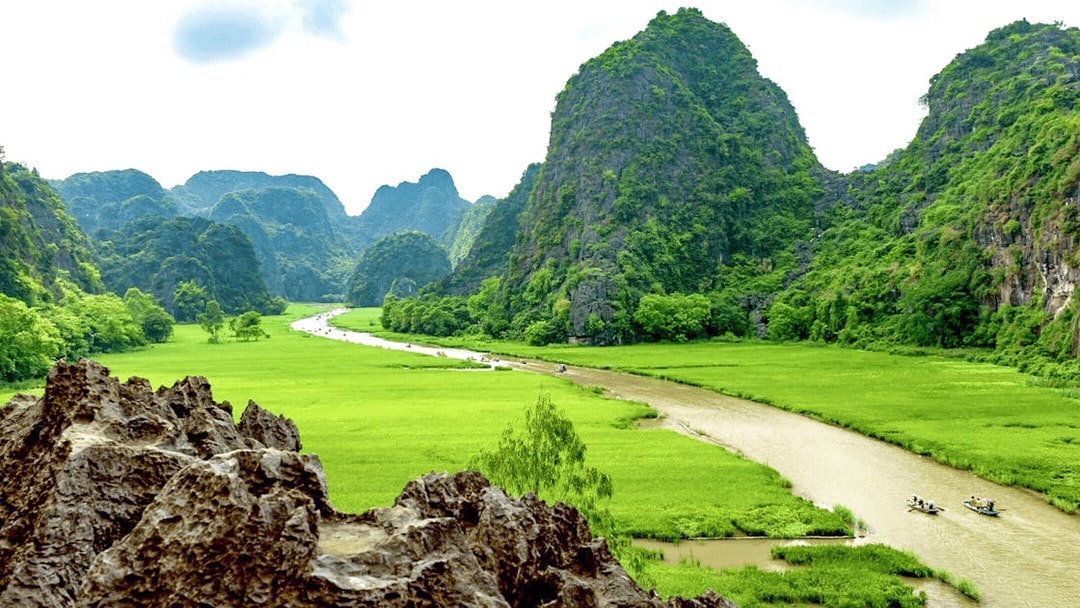 Boats on a river surrounded by lush green mountains in Tam Coc, Vietnam.