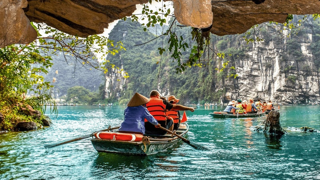 Boat tour through limestone caves in Tam Coc, Vietnam, with tourists rowing on a serene river.