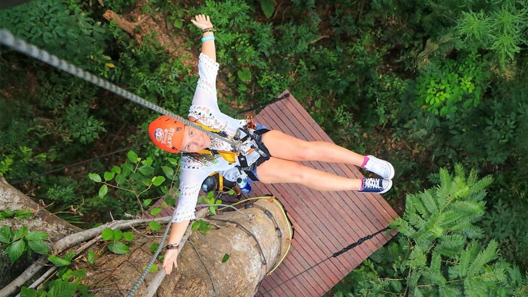 Lady ziplining at Hanuman World, Phuket, Thailand, surrounded by lush forest.