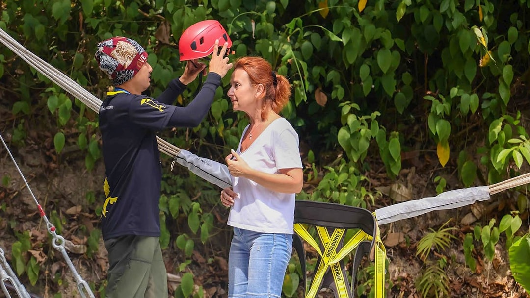 Guide assisting woman with helmet at Hanuman World zipline adventure.