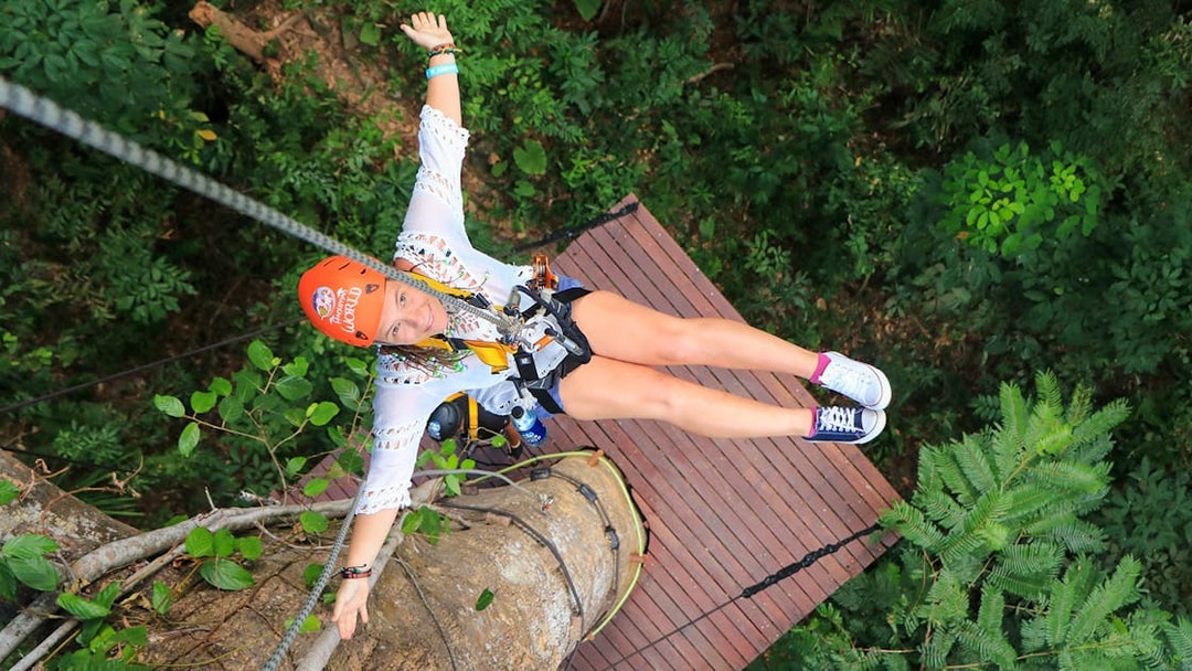Woman ziplining at Hanuman World, Phuket, Thailand, surrounded by lush greenery.
