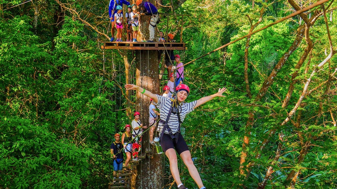 Tourist zip lining through lush forest at Hanuman World Zipline, Thailand.