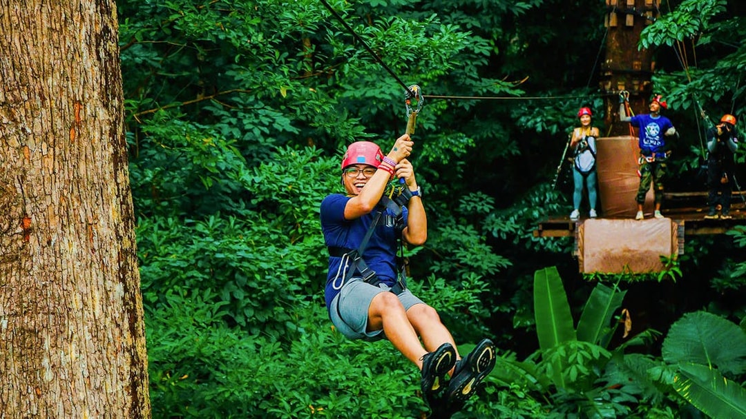 Tourist zip lining through lush forest at Hanuman World Zipline, Thailand.