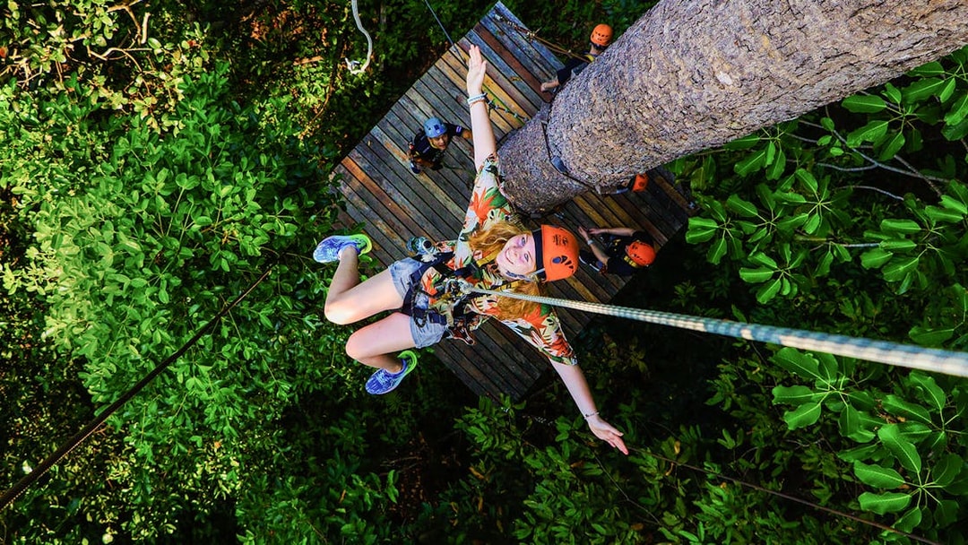Tourist zip lining through lush forest at Hanuman World Zipline, Thailand.
