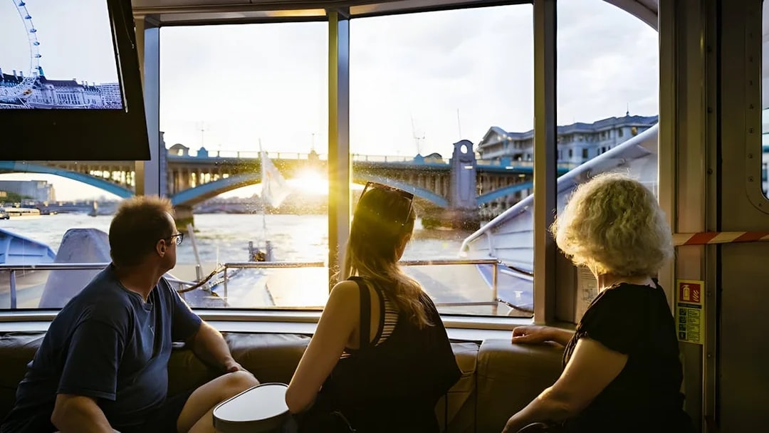People enjoying a river cruise view of London Bridge at sunset.