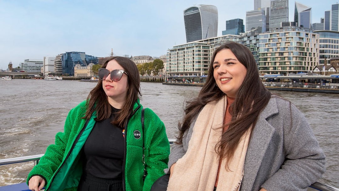 Women enjoying a Thames River afternoon cruise with London skyline in the background.