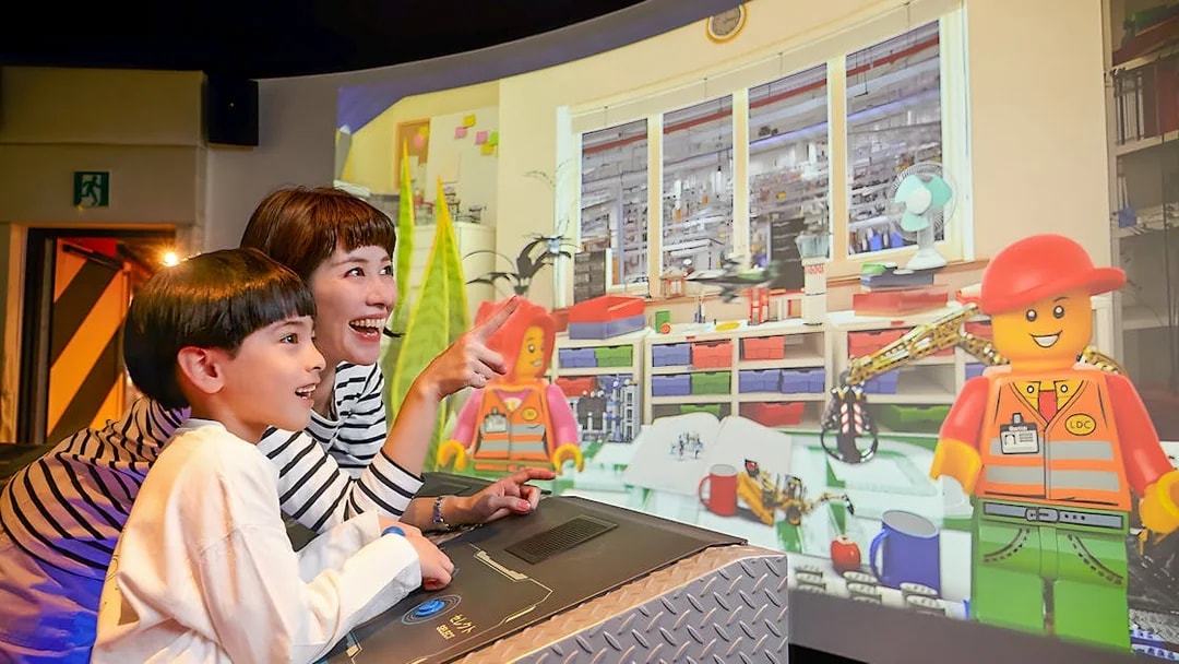 Child and adult enjoying interactive Lego display at Legoland Kansai.
