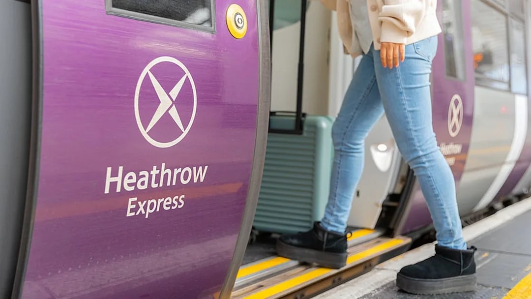 Person boarding Heathrow Express train with luggage at station.