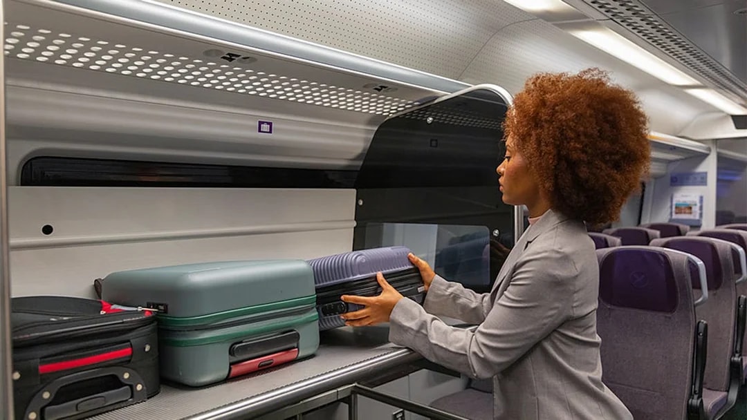 Passenger placing luggage in overhead compartment on Heathrow Express train to London Paddington.