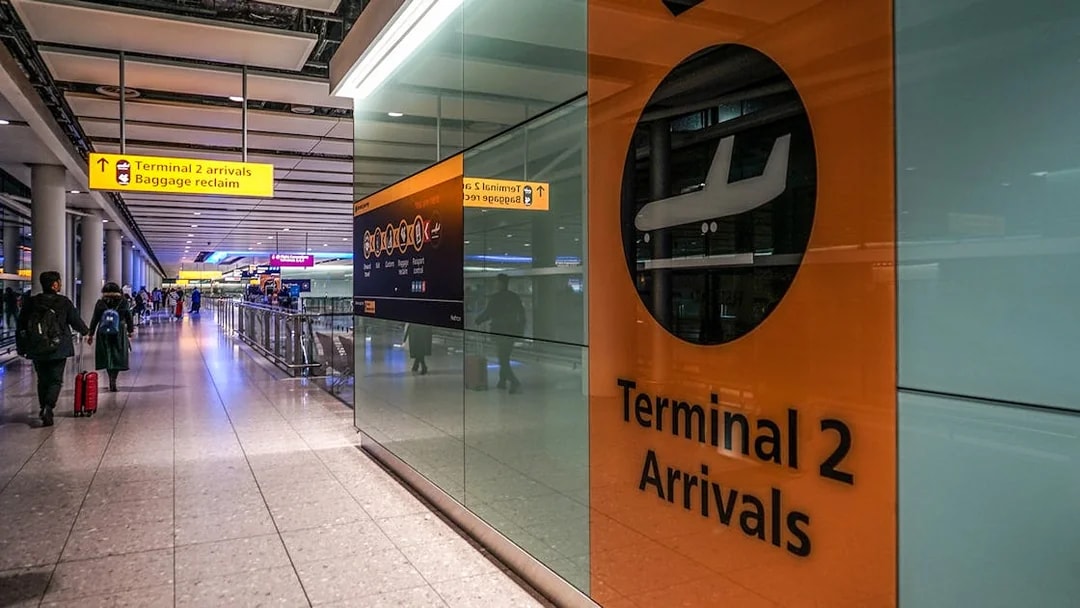 Heathrow Airport Terminal 2 arrivals area with passengers and signage.