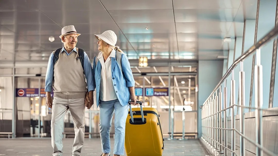 Senior couple with luggage walking through Heathrow airport terminal.