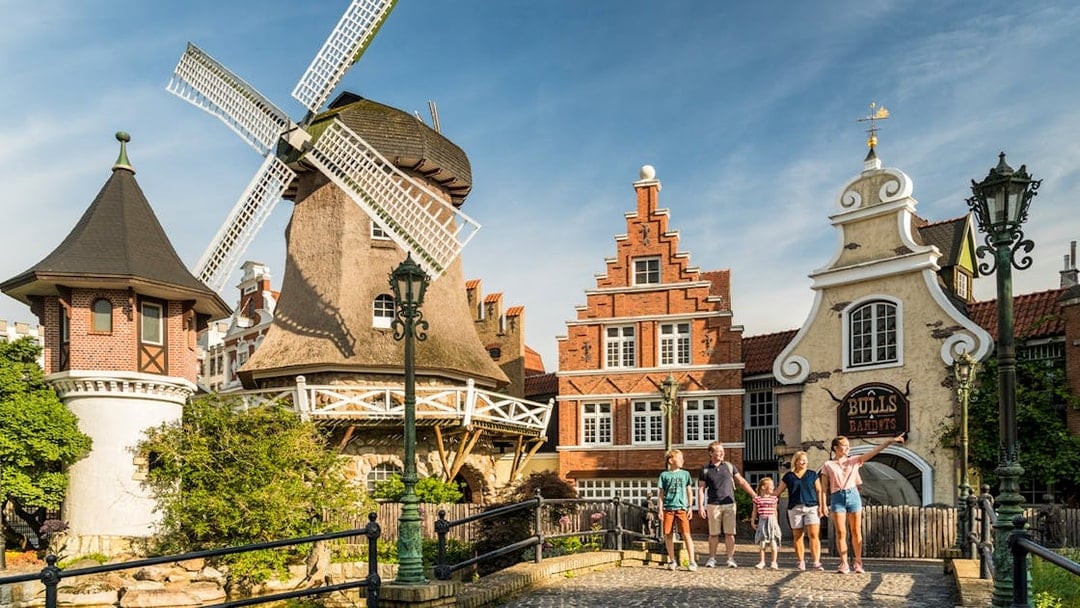 Family walking near windmill and historic buildings at Heide Park, Germany.