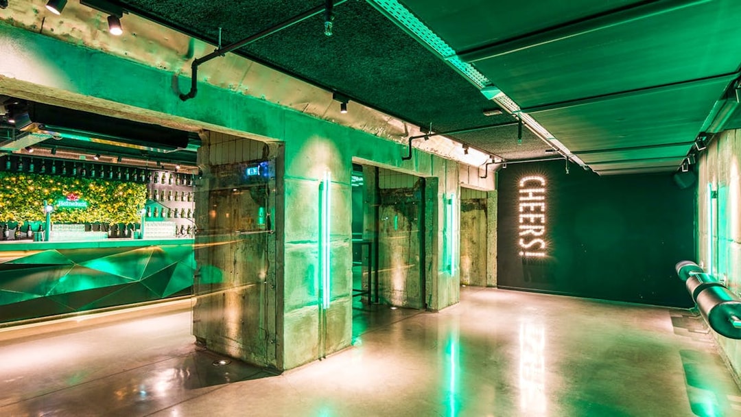 Heineken Experience bar area with green lighting and "Cheers" sign in Amsterdam.