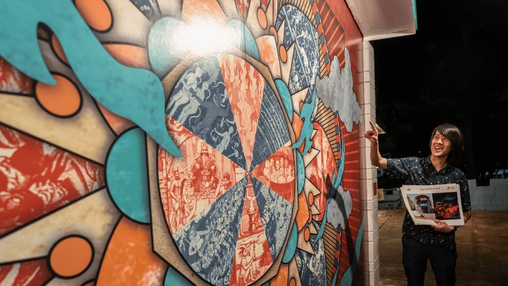 Tour guide gestures at colorful mural at Hell's Museum entrance, Singapore.
