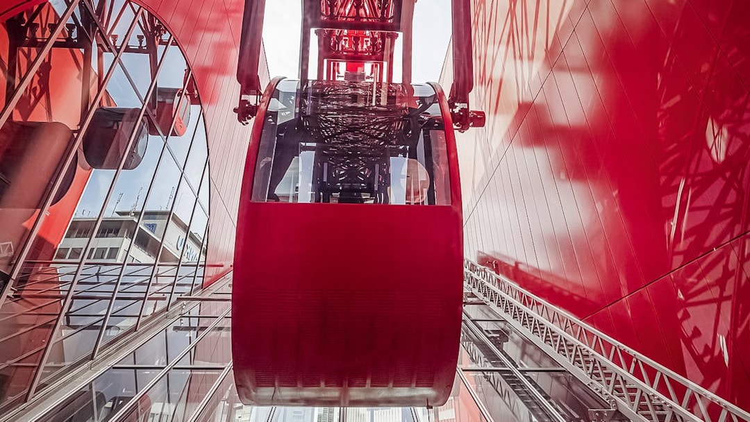 Red Ferris wheel cabin at HEP, viewed from below, with glass reflections.
