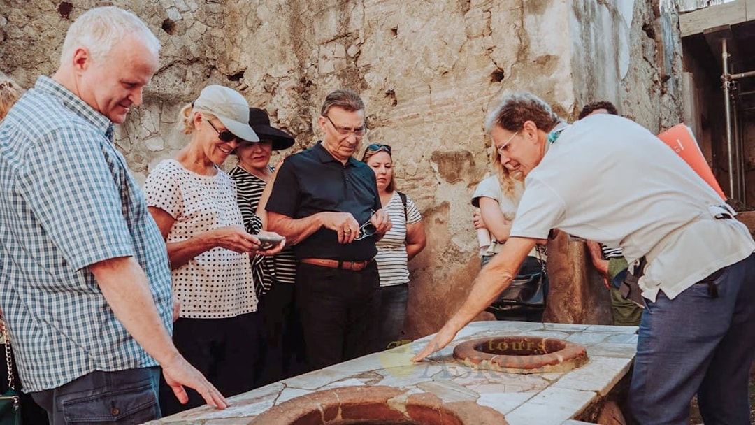 Group listening to archaeologist during Herculaneum guided tour, examining ancient ruins.