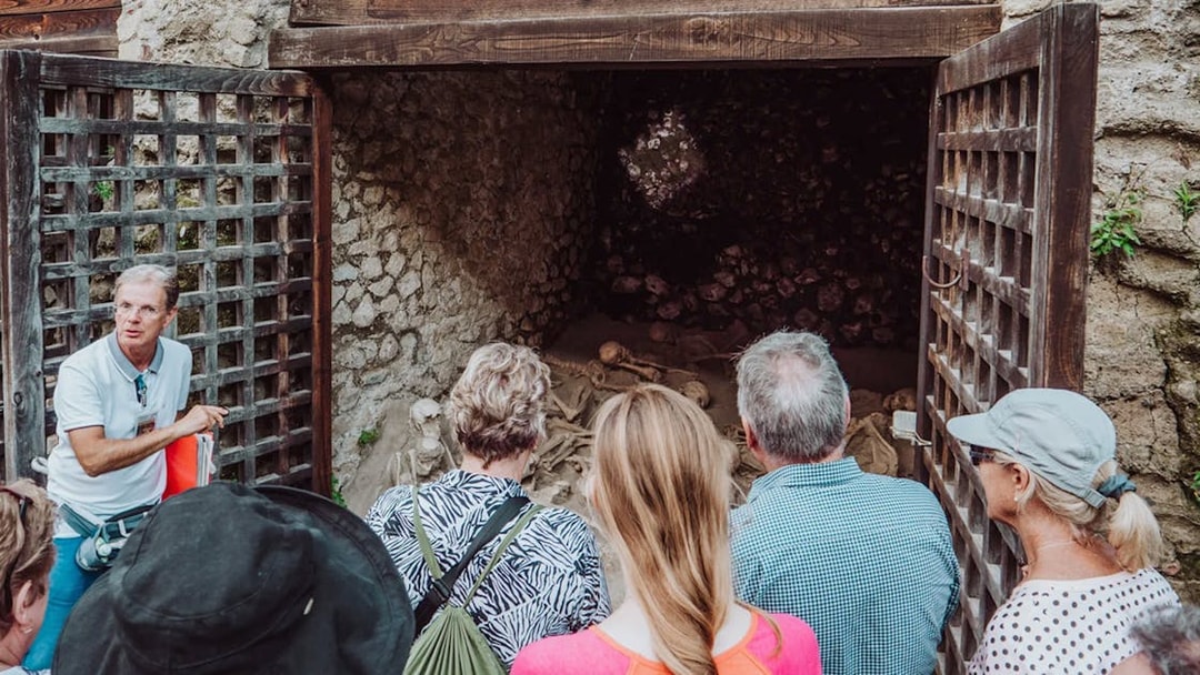 Tour group with archaeologist at Herculaneum site viewing ancient skeletons.