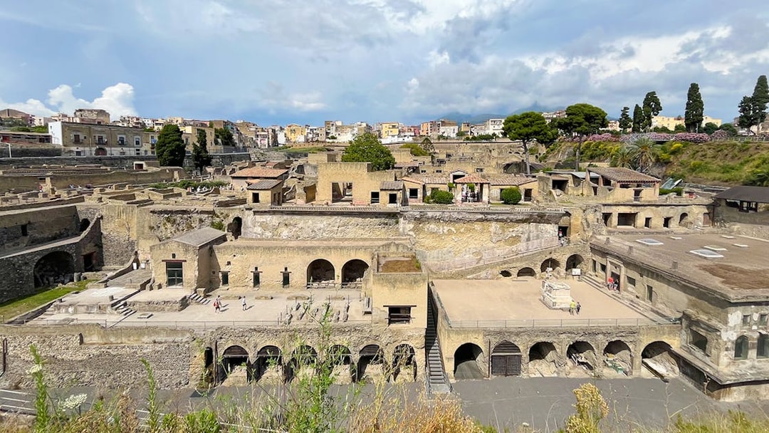Aerial view of ancient ruins in Herculaneum, Italy, with surrounding buildings and greenery.
