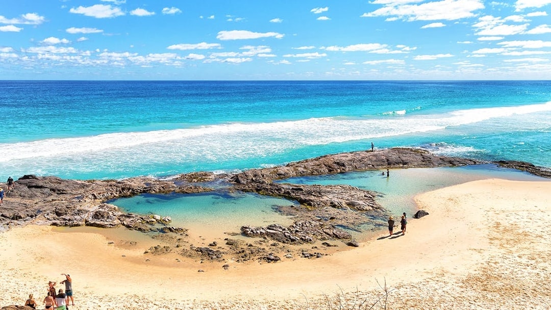 People exploring rock pools on K'gari (Fraser Island) beach during a guided tour.