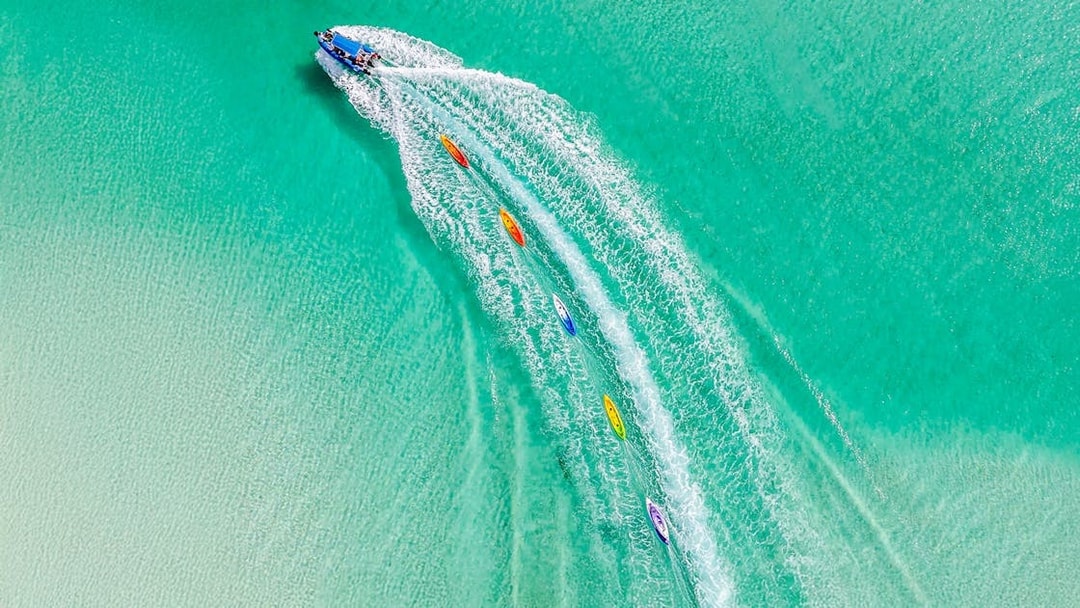 Aerial view of watersports activities on Fraser Island, K'gari, with kayaks trailing a speedboat.