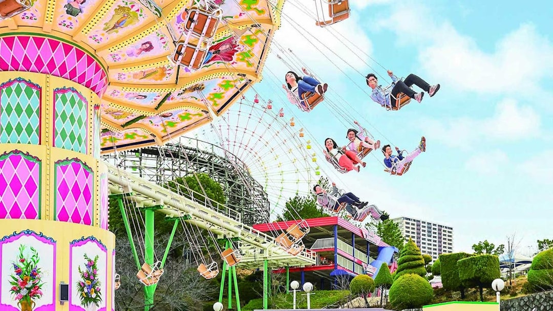 Visitors enjoying a swing ride at Hirakata Park, Japan, with a roller coaster in the background.