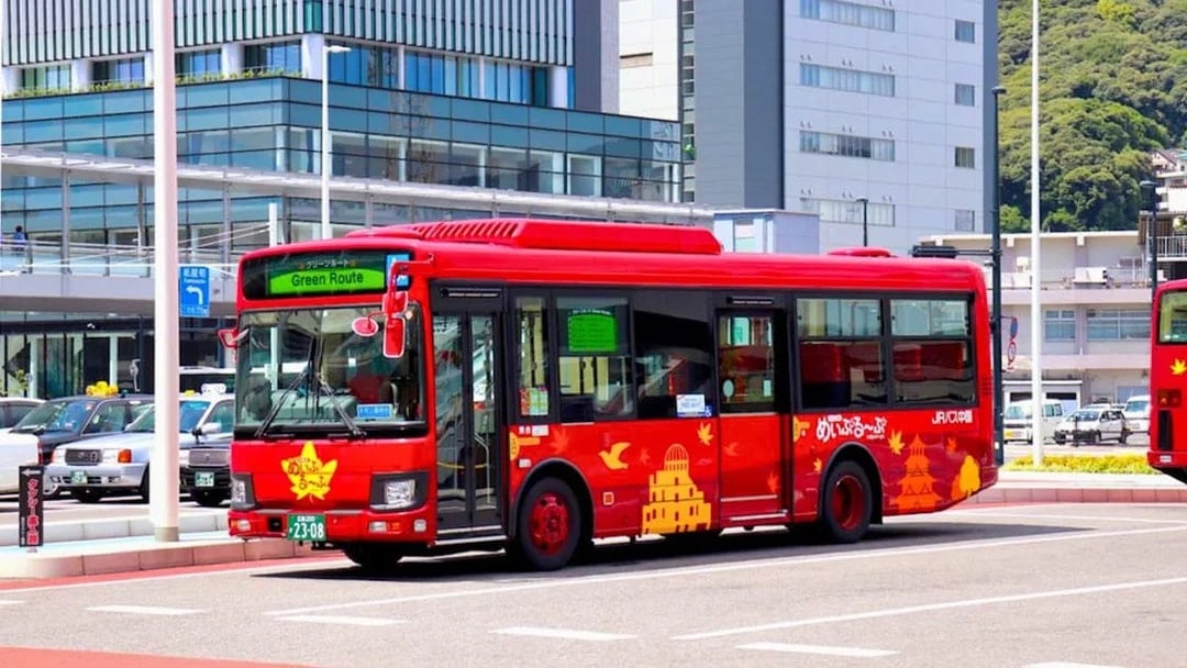 Red sightseeing bus on Hiroshima's Green Route near modern buildings.