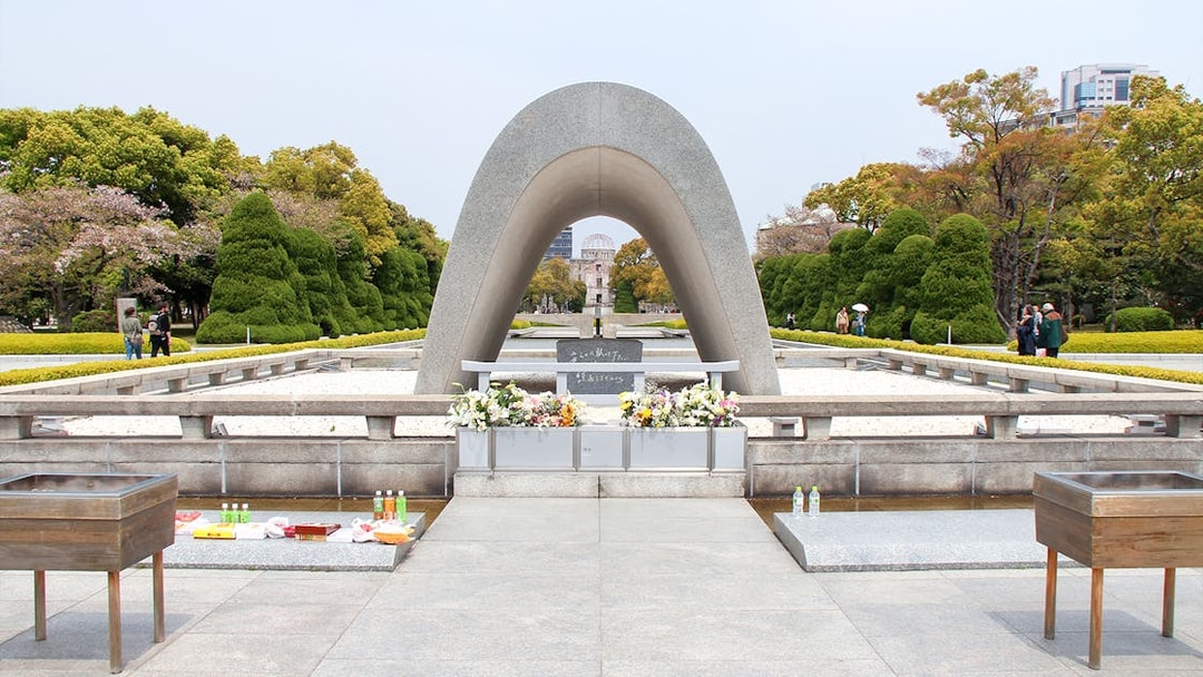 Hiroshima Peace Memorial Park cenotaph with flowers, view of Atomic Bomb Dome in background.
