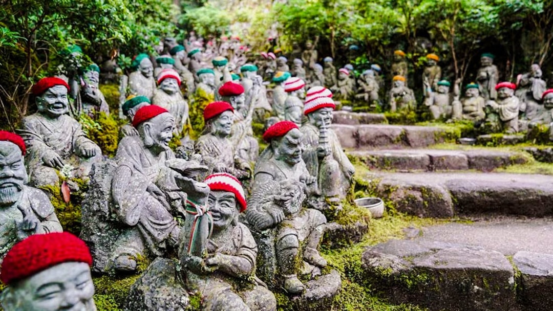 Stone statues with red hats at Daishoin Temple, Japan, surrounded by greenery.